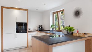 A modern kitchen with a central island, built-in appliances, and a large window providing natural light. - Falkenstein Apartment with Mountain View, Two Balconies, Private Sauna (Garmisch-Partenkirchen)