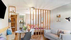 Uma sala de estar moderna com sofá, mesa de jantar com cadeiras, estante e cama separada por um painel de madeira.