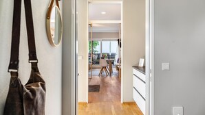 Corredor que leva a uma sala de jantar com uma mesa e cadeiras, um cabideiro e um espelho na parede.
