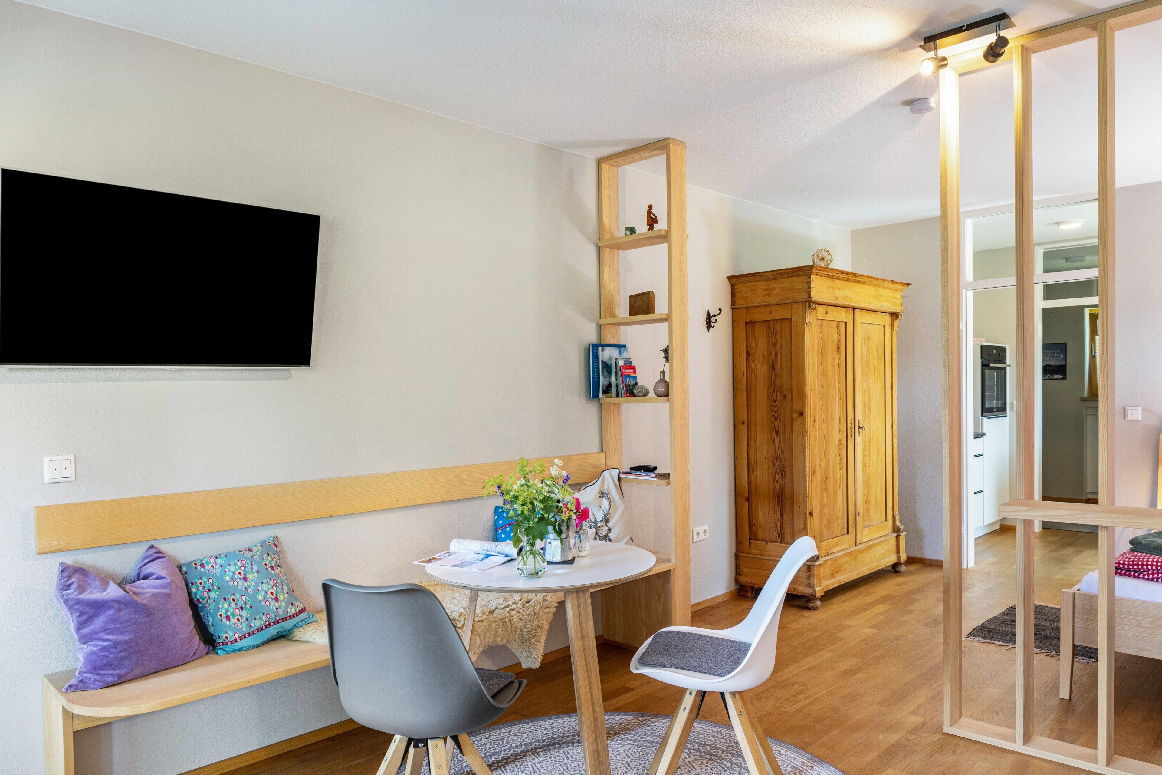 Una sala de estar moderna con un televisor de pantalla plana, un mueble de madera, una mesa de comedor con sillas y un banco con cojines.