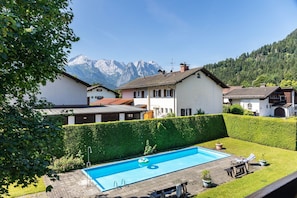 Une piscine dont le décor est constitué par une chaîne de montagnes, entourée de haies soigneusement taillées et surplombée par un ciel dégagé.