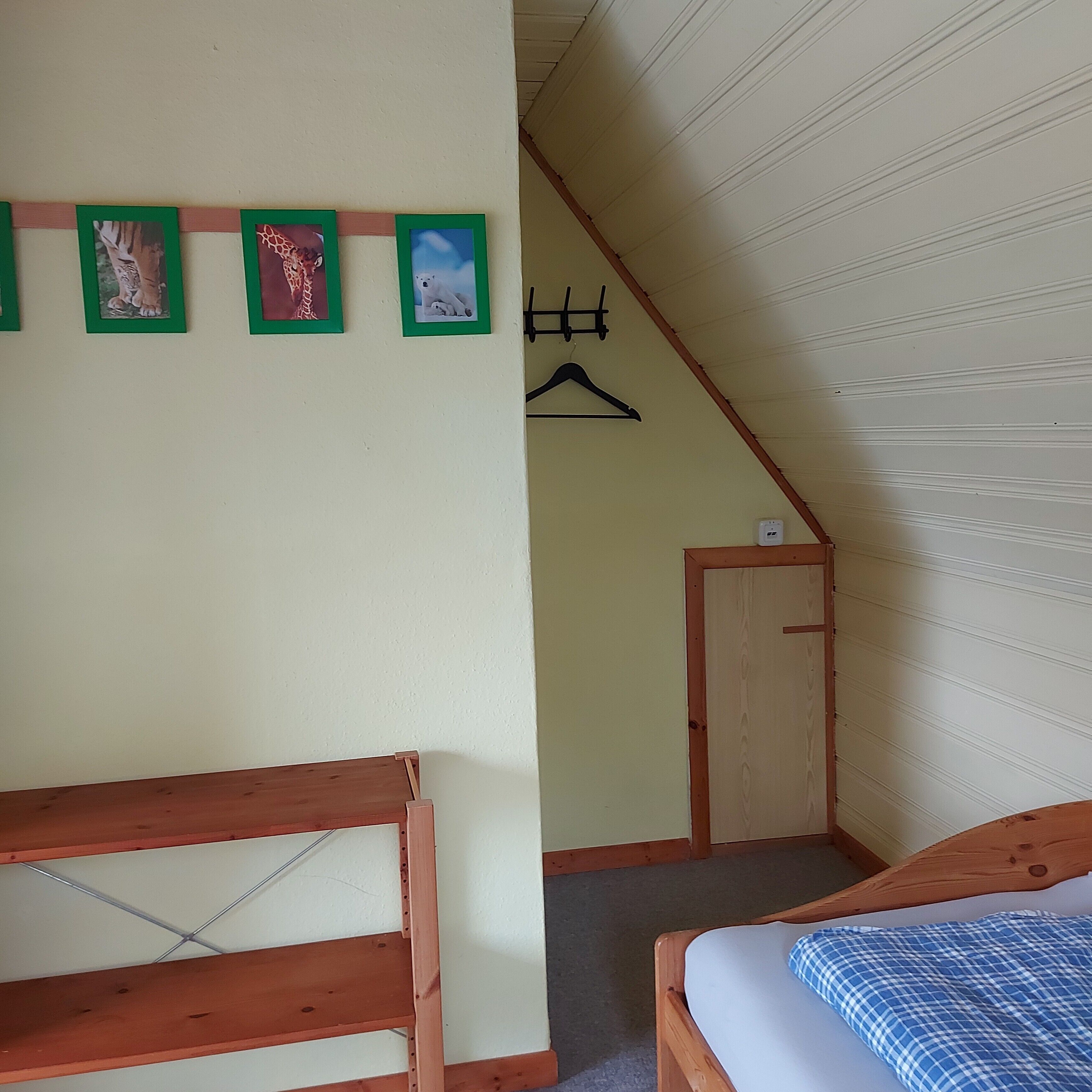 Una habitación con una cama de madera, una mesita de madera, un perchero en la pared y una puerta.