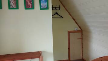 Una habitación con una cama de madera, una mesita de madera, un perchero en la pared y una puerta.