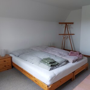 Ein Schlafzimmer mit einem Bett, einem Holzkleiderschrank und einer Staffelei mit Kleidung.