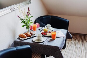 A breakfast table with croissants, fruit, juice, and a vase of flowers.
