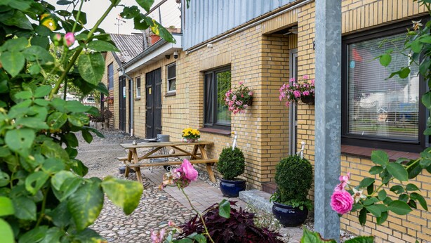 Ein Backsteinhaus mit einer Holzbank, Blumentöpfen und hängenden Blumenkörben.