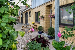 Un bâtiment en briques avec un banc en bois, des plantes en pot et des jardinières suspendues.