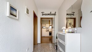 Ein Flur mit Fliesenboden, einem Spiegel, einem Schminktisch mit Lampe und einer Tür zu einer Küche.