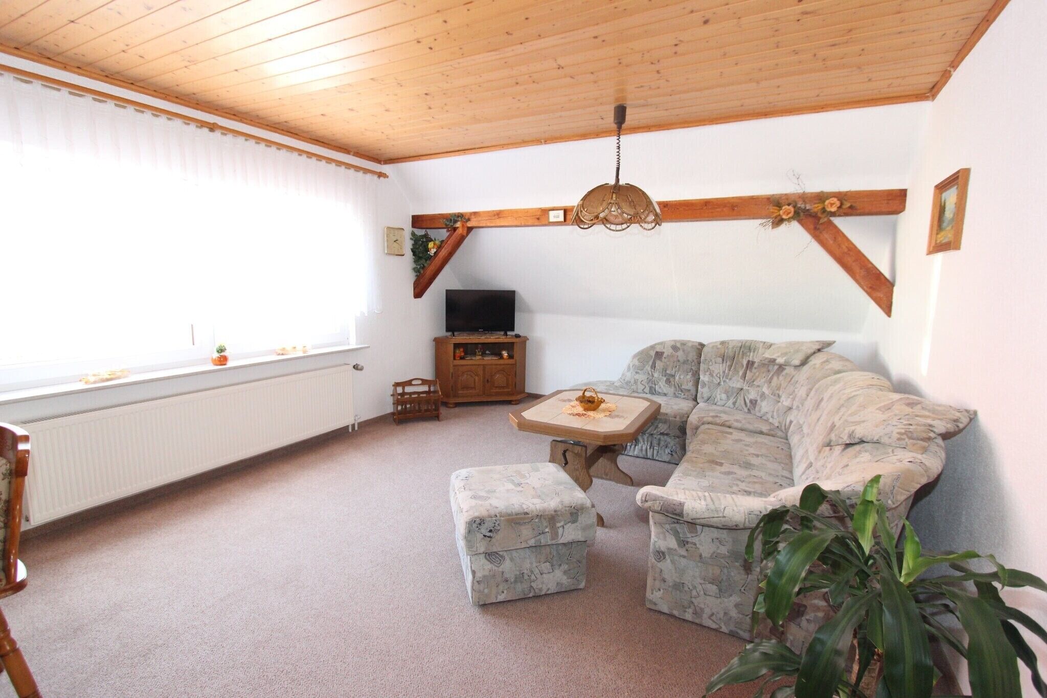 A cozy living room with a wooden ceiling, a sofa, a small table, and a television.