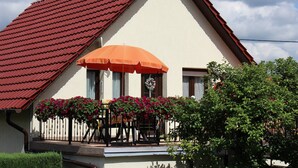 Et hus med røde tegltage, en balkon med bord og stole, og en blomsterkasse med røde blomster.