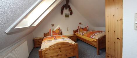 A small attic bedroom with two wooden beds, a sloped ceiling, and a radiator.