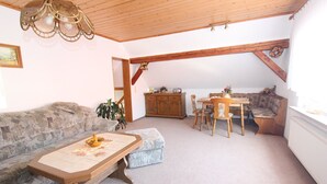 En hyggelig stue med en stensofa, et træbord som sofabord og et spiseområde med et træbord og stole.