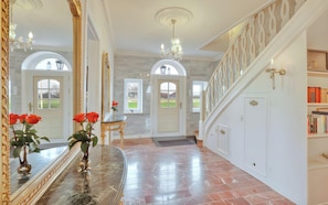 A grand hallway with marble flooring, a large mirror, a chandelier, and a staircase with a decorative railing.