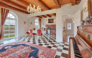 A dining area with a checkered floor, red and gold chairs, a chandelier, and a piano.