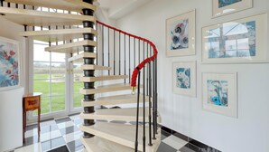 Un escalier en colimaçon avec une rampe rouge, un sol à carreaux et des œuvres d’art encadrées accrochées aux murs.