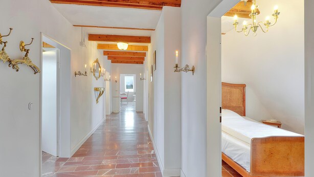 Un couloir d’hôtel avec un plafond en bois, un lit avec une tête de lit en bois et des appliques murales.