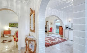 Un intérieur spacieux avec des plafonds en forme d’arc, une cheminée, un fauteuil rouge recouvert de tissu et un coin cuisine.