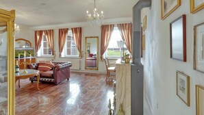Ein geräumiges Wohnzimmer mit Kamin, einer Chandelierleuchtre und einem Essbereich mit Tisch und Stühlen.