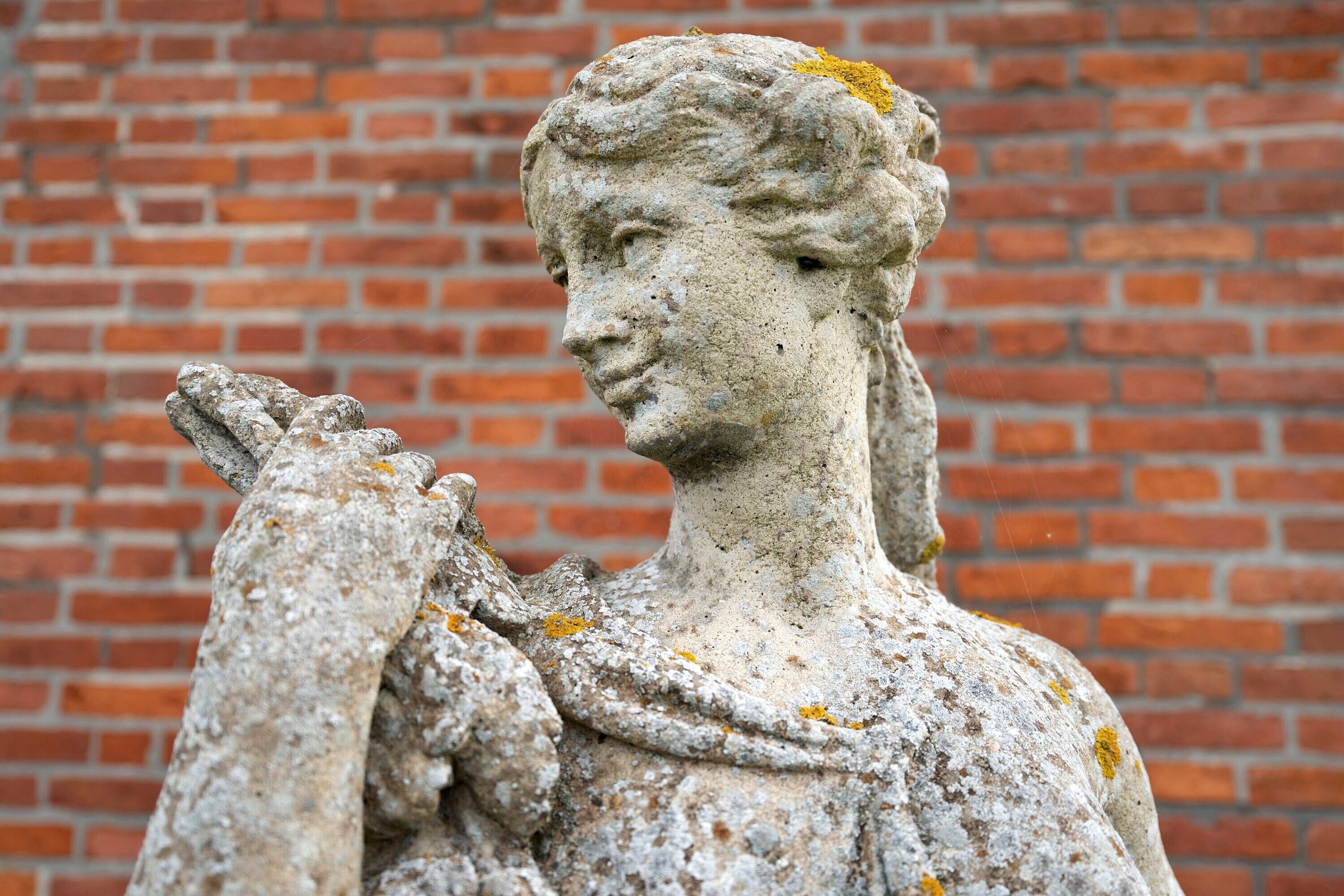 Una statua di pietra con un drappo, sullo sfondo di un muro in mattoni.