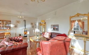 A luxurious living room with a fireplace, leather sofas, a round coffee table, and a large ornate mirror.