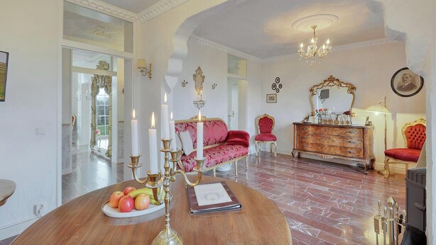 A room with a round wooden table, a red sofa, a wooden dresser, and a chandelier.