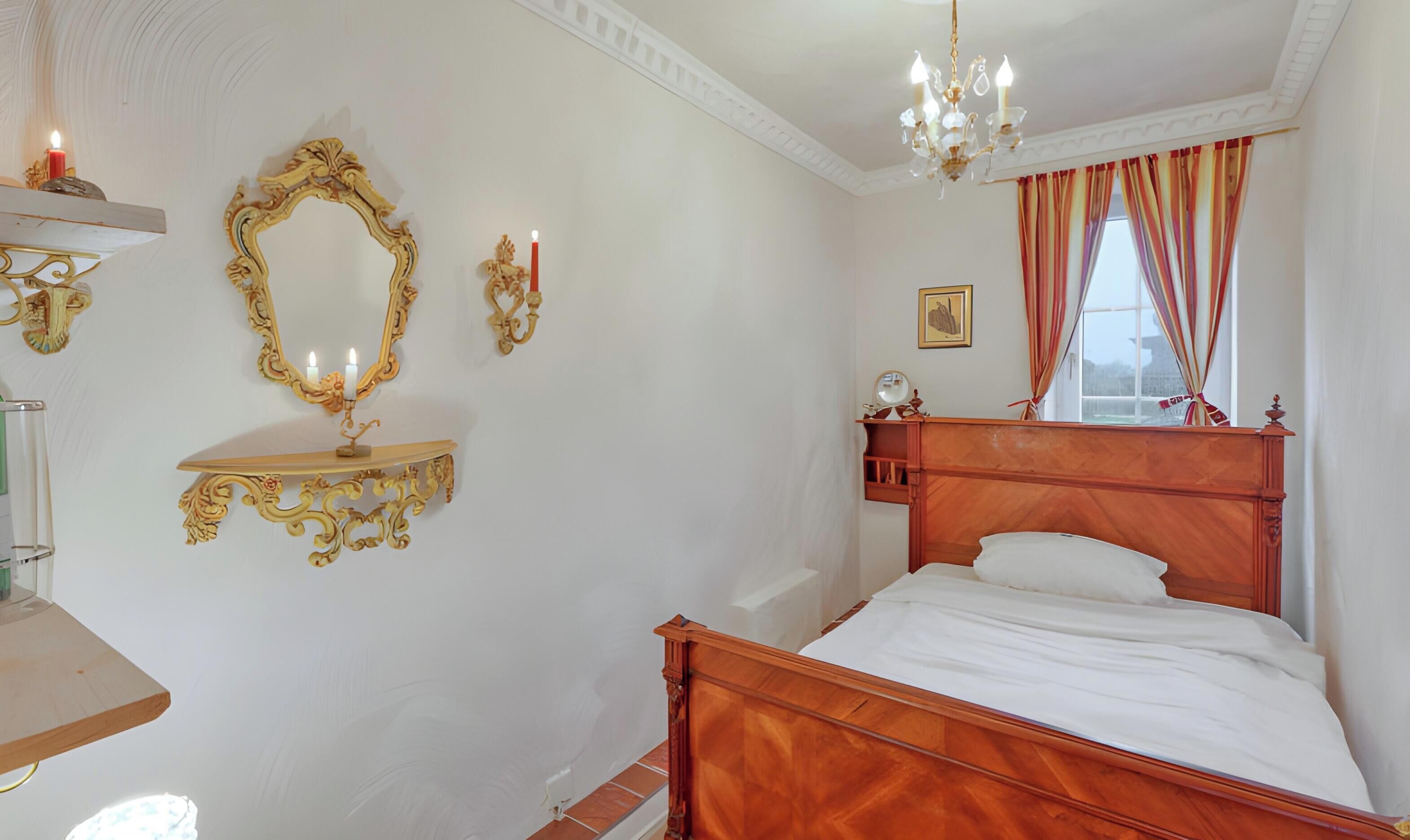 Une chambre à coucher avec un lit en bois, des miroirs décoratifs sur les murs, un lustre et une fenêtre avec des rideaux.