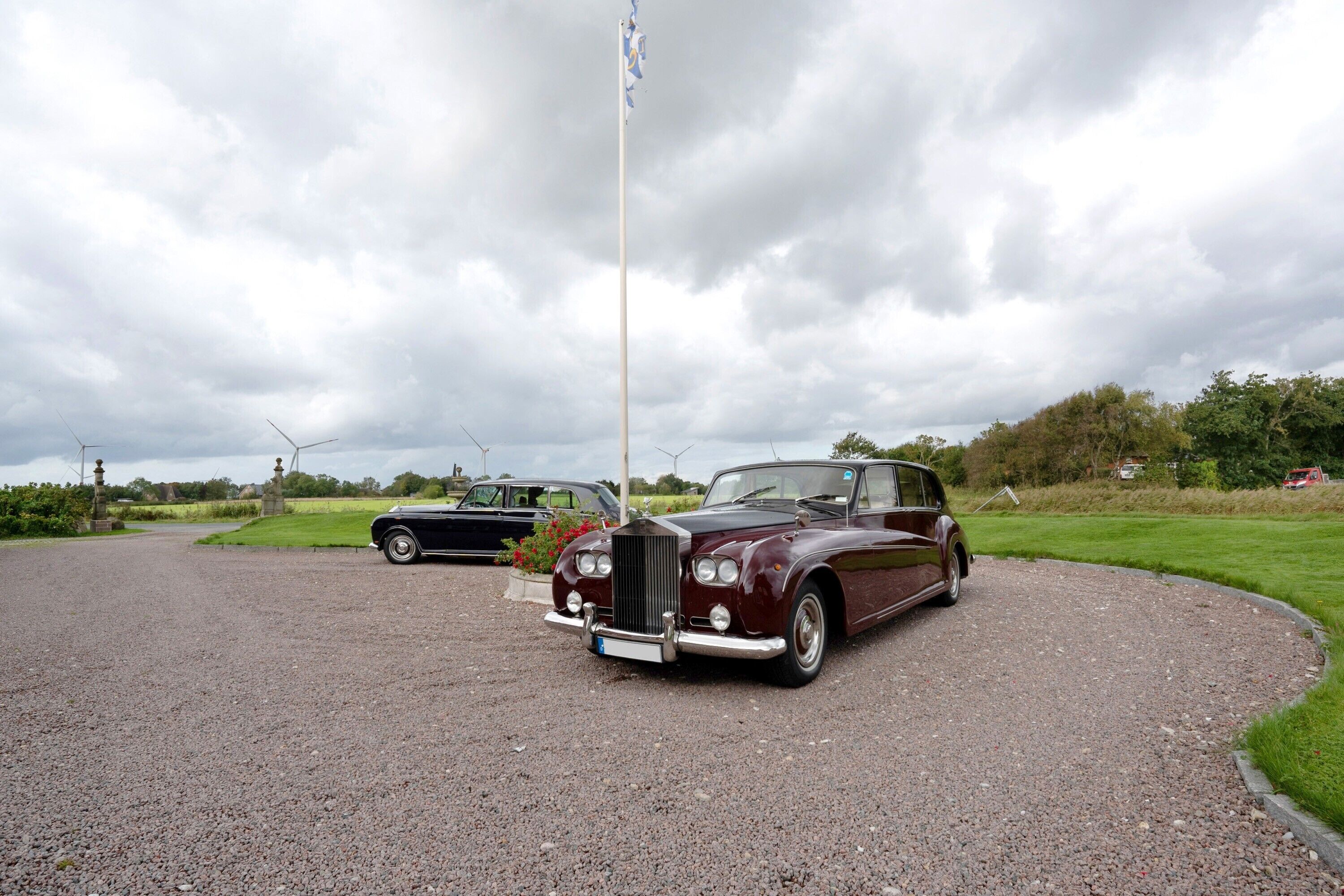 A vintage car parked on a gravel driveway with a grassy area and trees in the background.