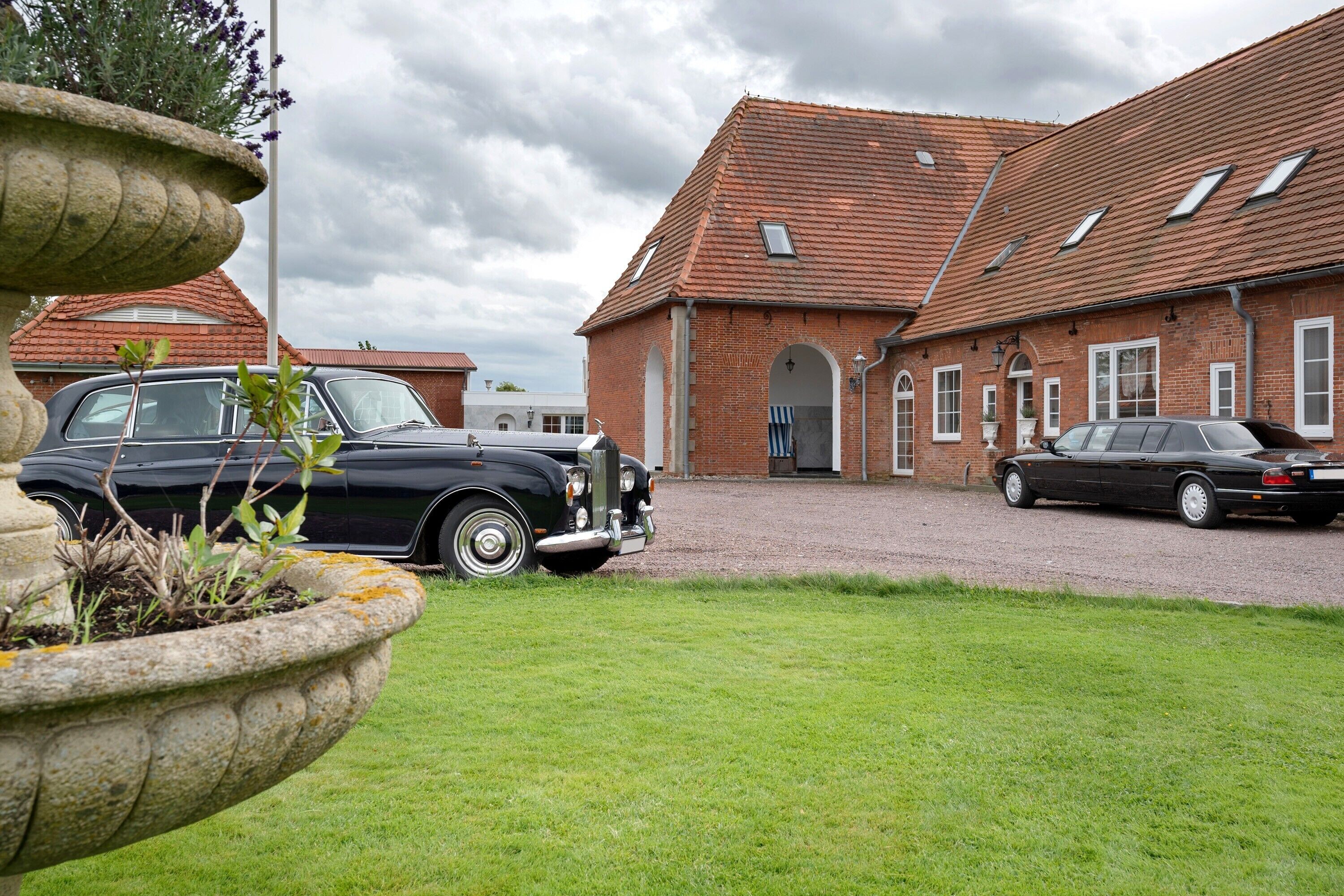 A courtyard with a fountain, two vintage cars, and a brick building with a tiled roof.
