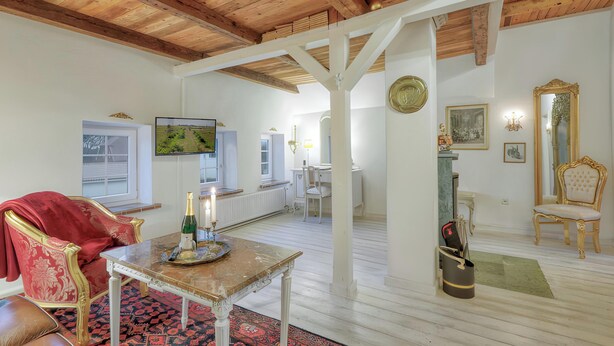 A room with a wooden ceiling, a table with a bottle, a red chair, a white chair, a mirror, and a painting on the wall. - Apartment 'Junior Suite' with Shared Garden and Wi-Fi (Emmelsbüll-Horsbüll)