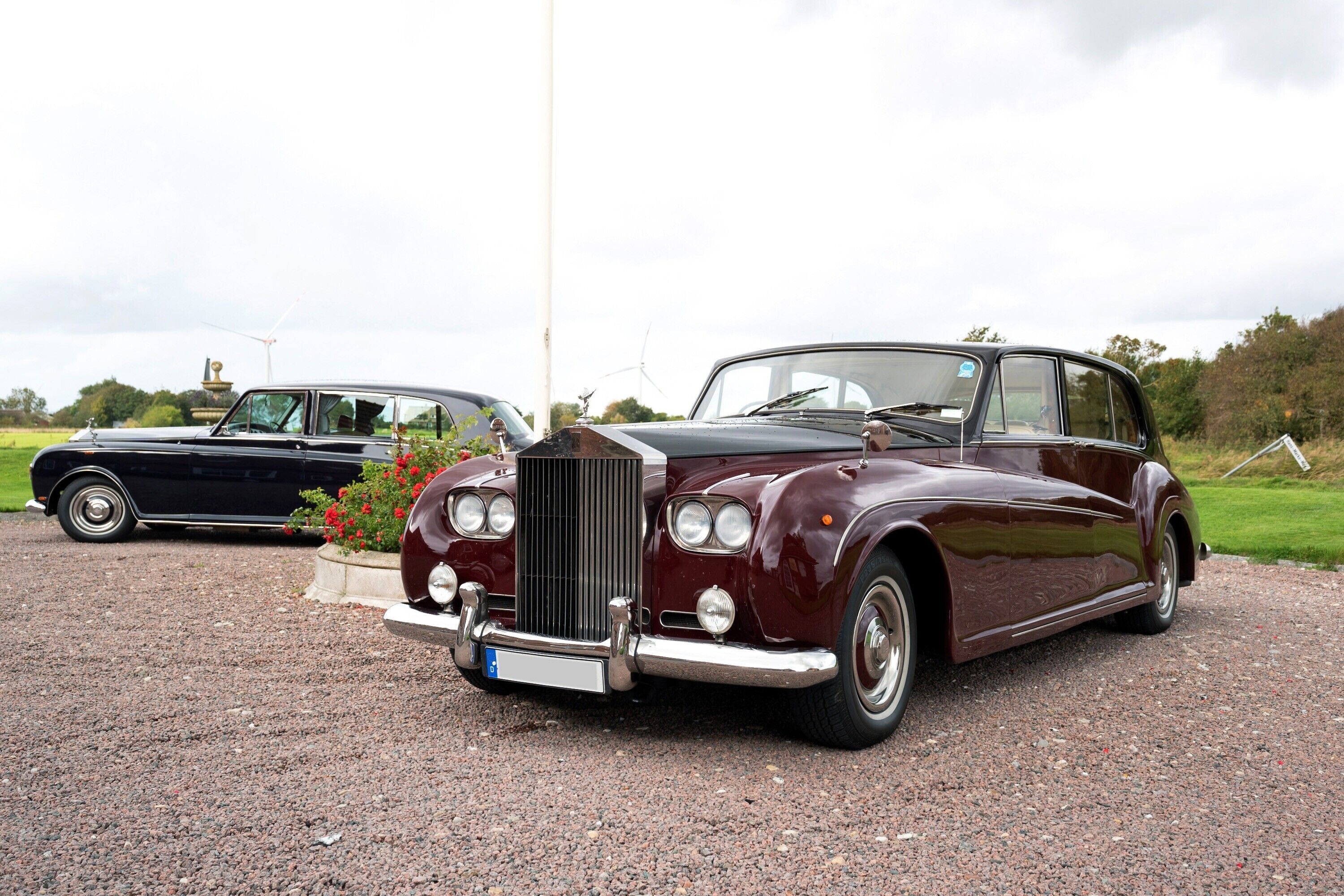 A vintage car parked on a gravel surface with a garden in the background.