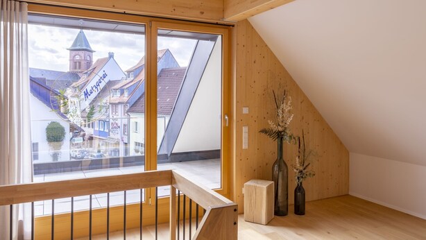 A room with a wooden ceiling, a large window with a view of a town, and a wooden floor. - Apartment 'Anna' with Shared Terrace, Balcony and Wi-Fi (Elzach)