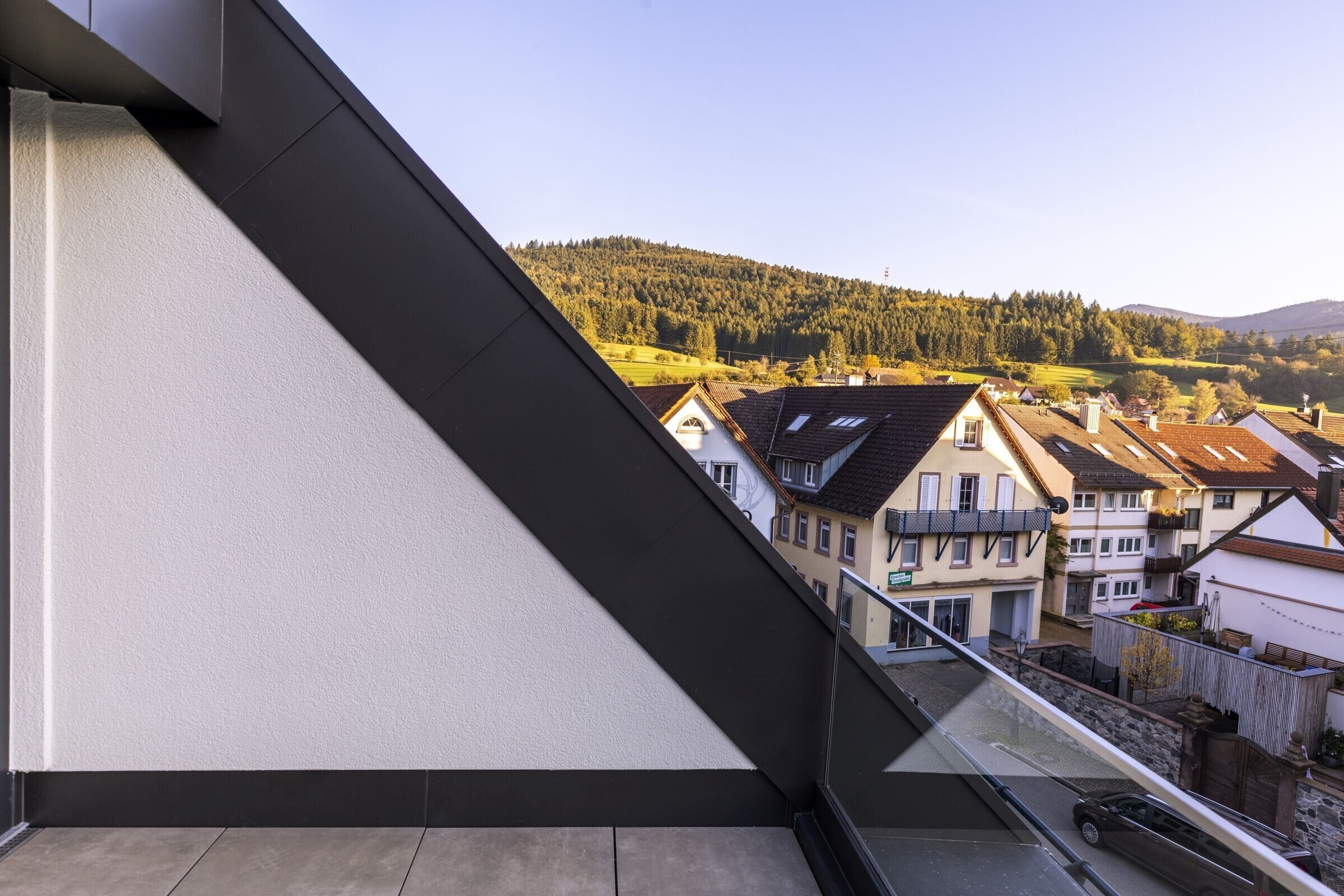 A balcony with a view of a residential area, a clear sky, and a hilly landscape in the distance.