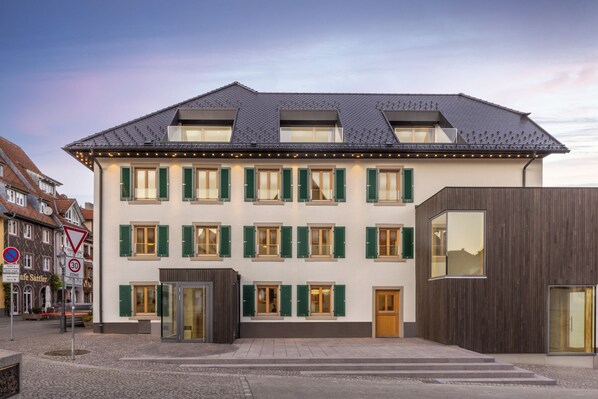 Ein mehrgeschossiges Gebäude mit flachem Dach, grünen Fensterläden und einer modernen Fassade.