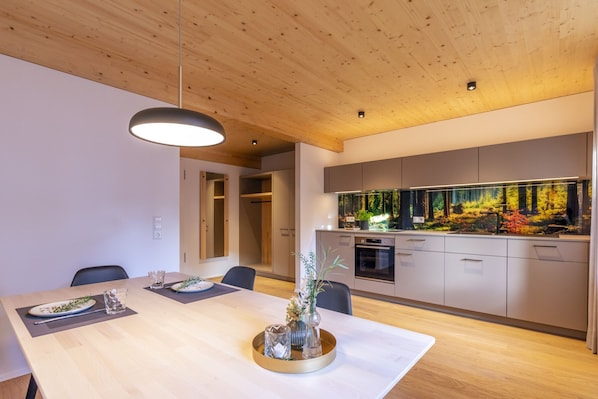 Une cuisine moderne dotée d’un aquarium intégré, d’un plafond en bois et d’un coin repas avec une table dressée pour deux personnes.