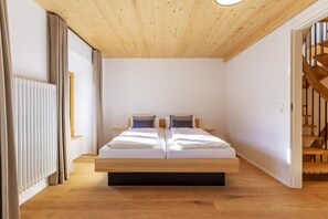 Une chambre avec un plafond en bois, un lit avec une literie blanche, un radiateur et un escalier.