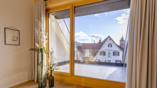 A room with a large window, wooden flooring, and two vases with dried plants.