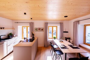 Une cuisine moderne dotée d’un îlot central, d’un coin repas avec une longue table et de grandes fenêtres.