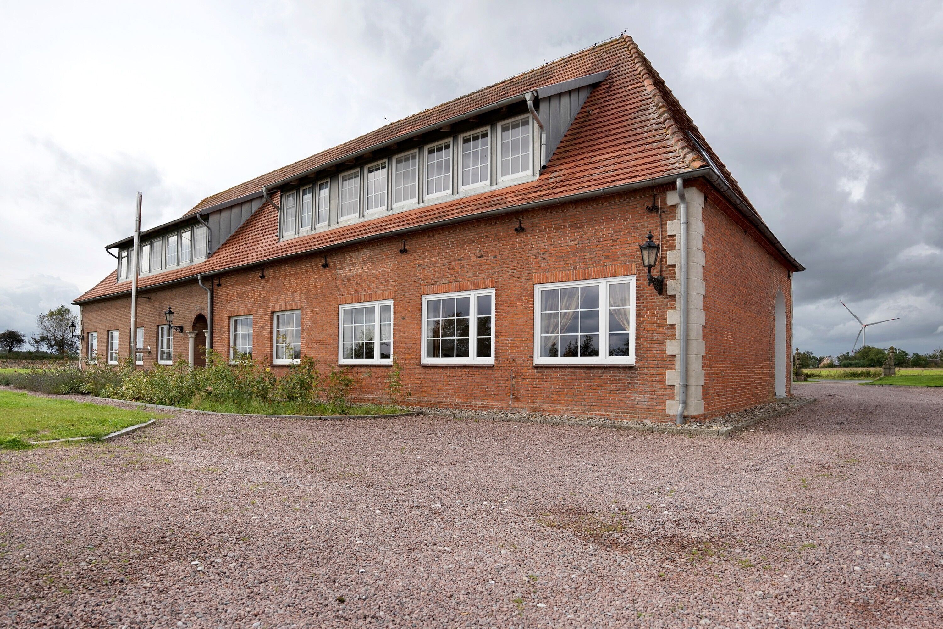 A two-story brick building with a sloped roof, multiple windows, and a gravel driveway.