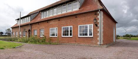 A two-story brick building with a sloped roof, multiple windows, and a gravel driveway.