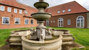 A courtyard with a stone fountain featuring lion sculptures, a brick building with arched windows, and a well-maintained lawn.