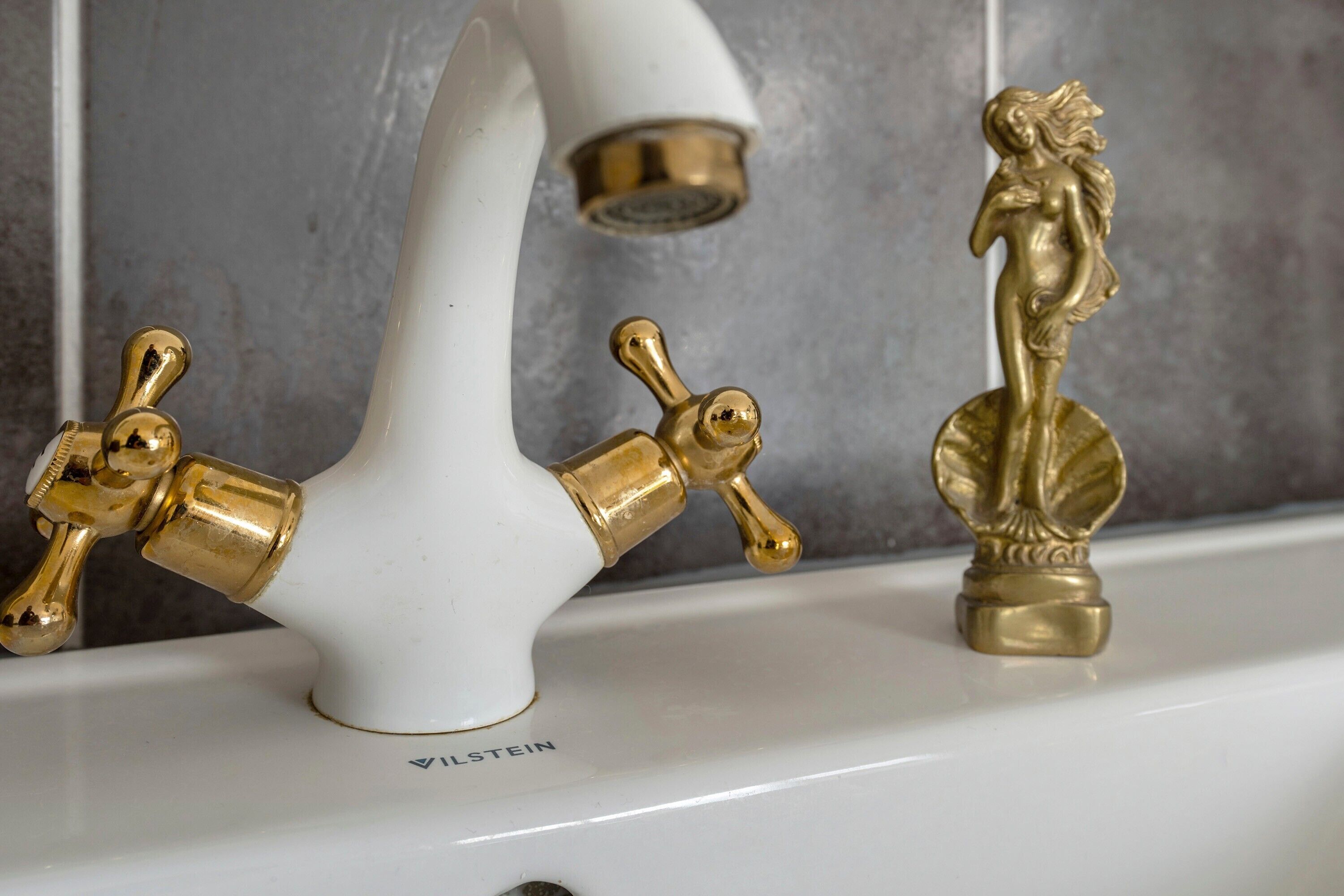 Un baño con un lavamanos blanco, dos grifos dorados y una figura decorativa dorada.