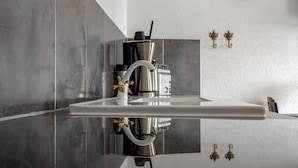 Una cocina moderna con una cafetera de acero inoxidable, una encimera blanca y un grifo de pared.