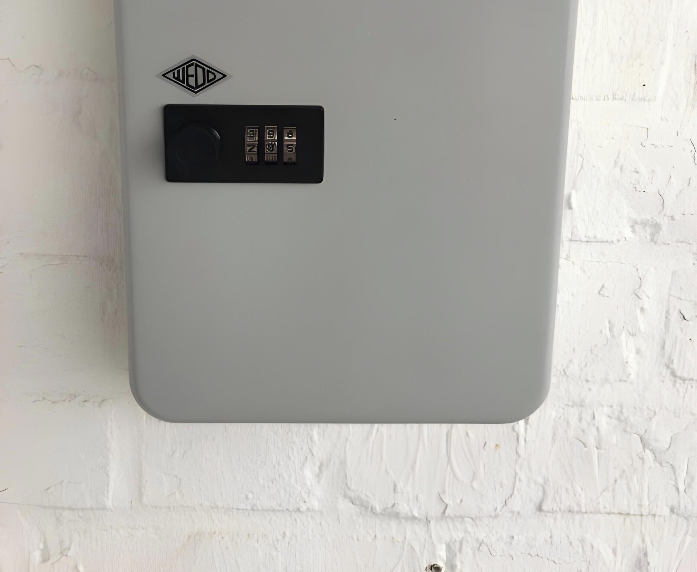 Pared de cinza com padrão de tijolos brancos e um objeto retangular preto com um logo em formato de diamante e três botões.