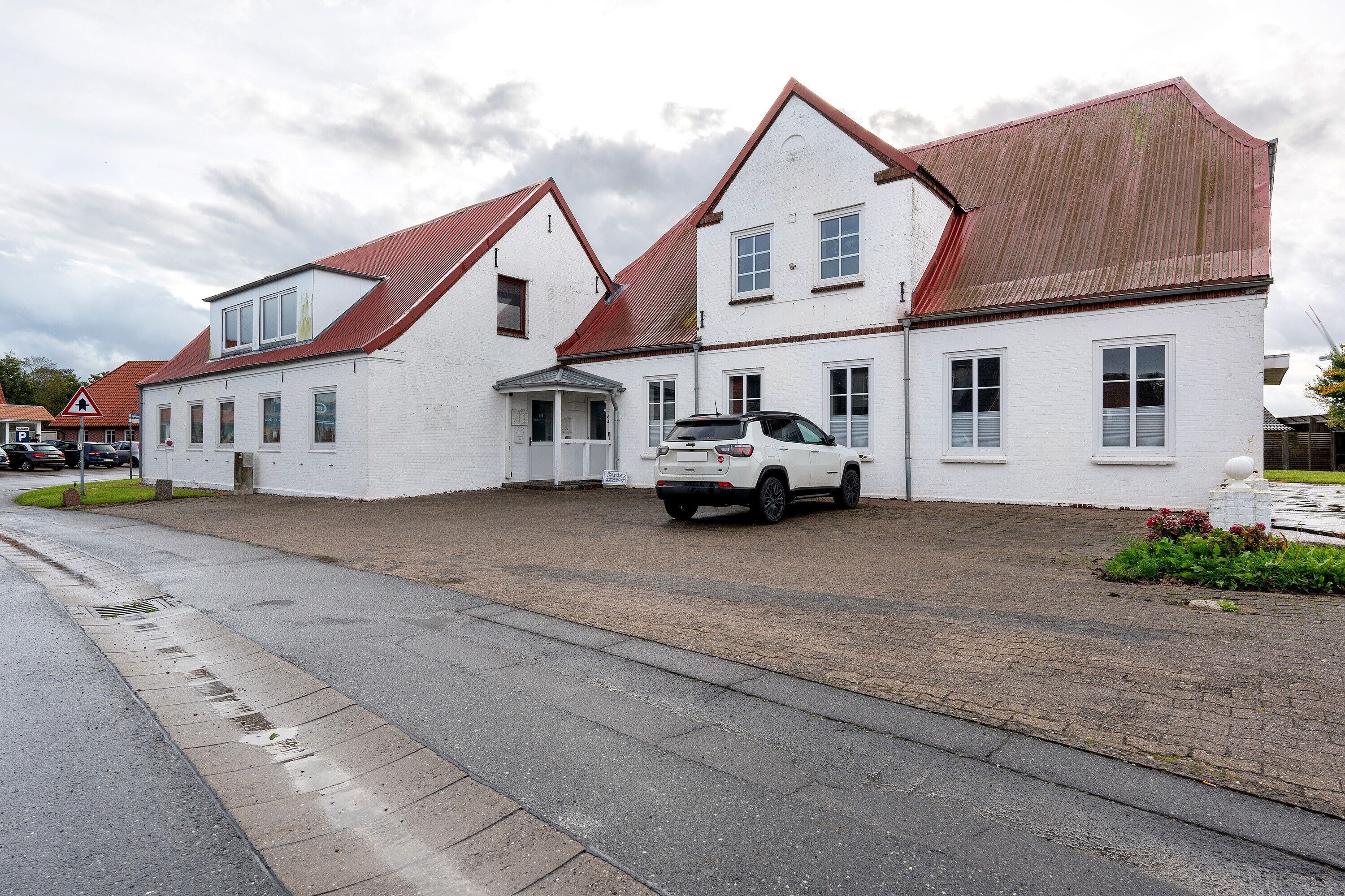 A two-story white building with a red roof, a driveway, and a parked white car.
