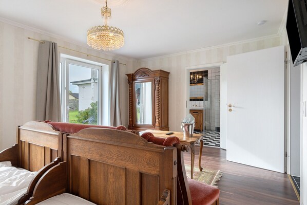 A bedroom with a wooden bed, a chandelier, a large mirror, and a view of the outside.
