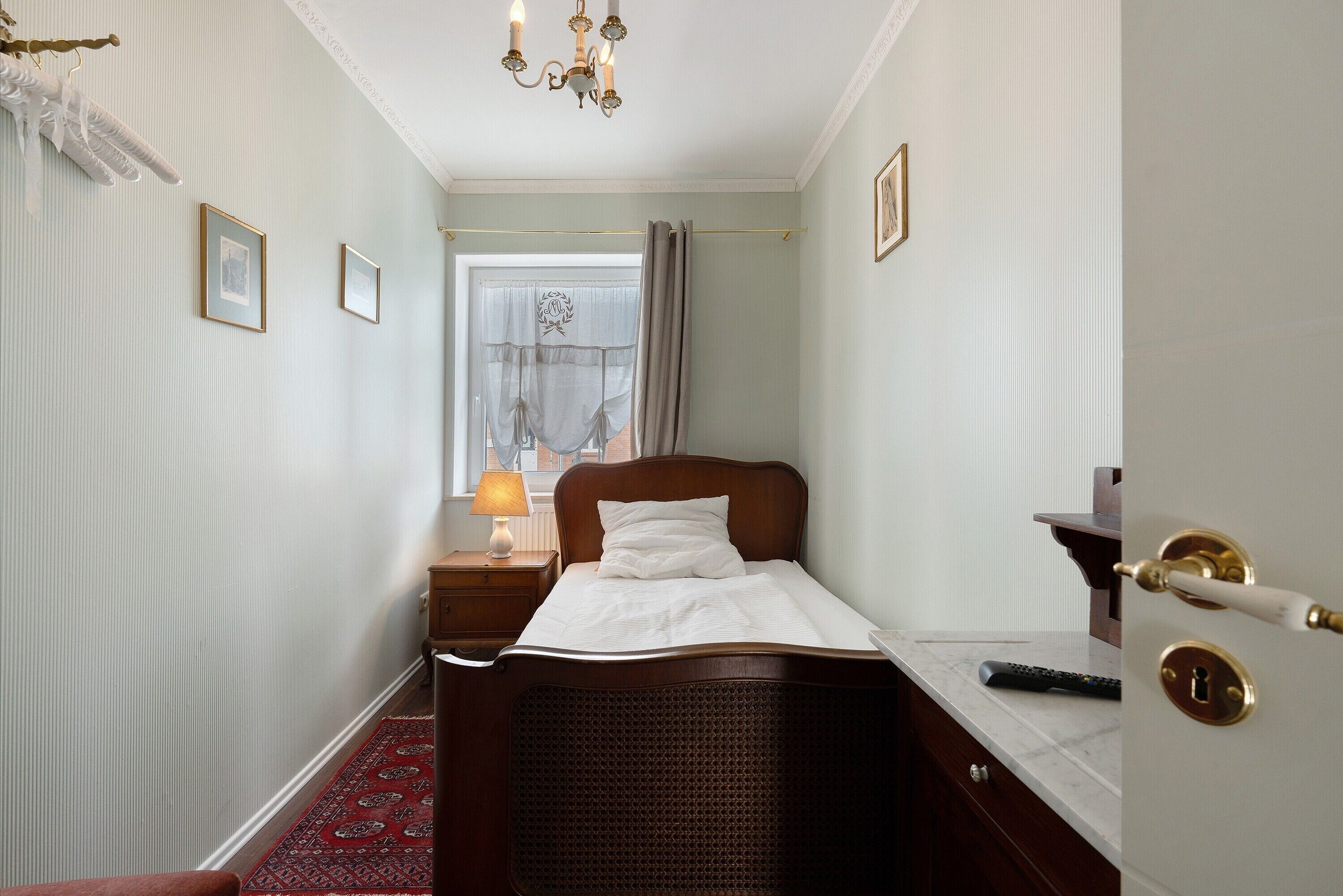 Quarto bem arrumado com cama, mesa de cabeceira, abajur e janela com cortinas.