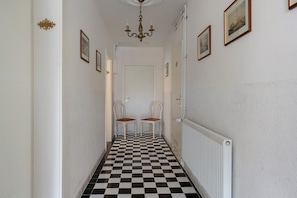 A hallway with a checkered floor, two chairs, a radiator, and framed pictures on the walls.