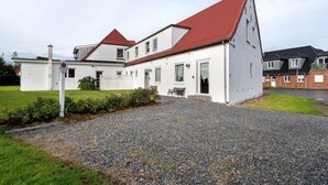 A white building with a red roof, a gravel driveway, and a small garden area.