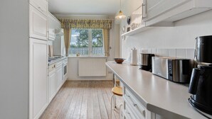 Una cocina con armarios blancos, una ventana con cortinas, un radiador, un tostador y una tetera.