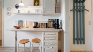 Una cocina con cubierta blanca, dos taburetes, un tendedero y diversos electrodomésticos.